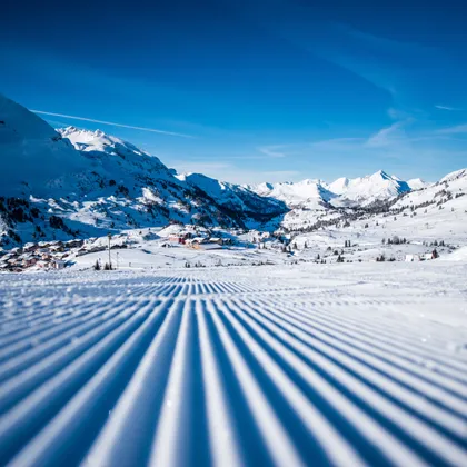 Groomed ski slope in snowy Alps under clear blue sky